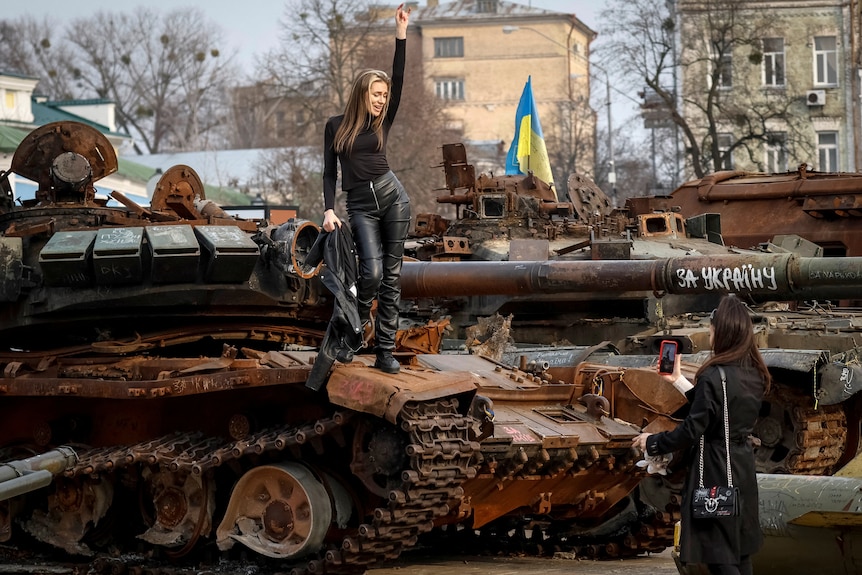 A woman poses for a photo while standing on a Russian tank and dressed in black.