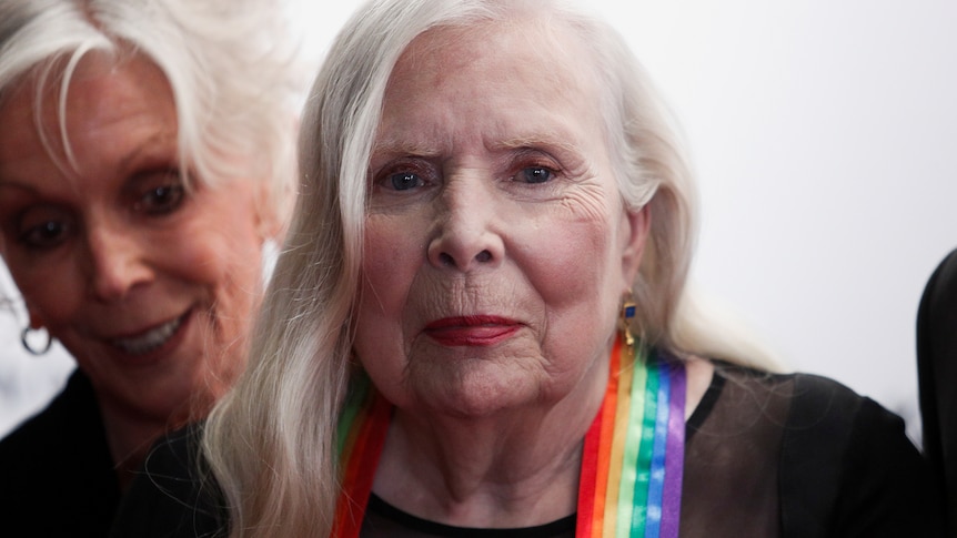 a close up image of Joni Mitchell wearing the rainbow ribbon of the Kennedy Center Honors with another woman beside her