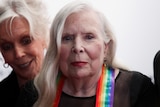 a close up image of Joni Mitchell wearing the rainbow ribbon of the Kennedy Center Honors with another woman beside her