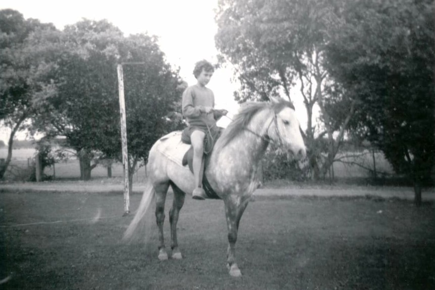 Black and white photo of Ewart as a young girl sitting on the back of a horse.