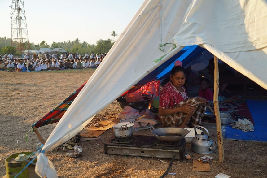 Woman preparing a meal while Muslims pray in a soccer field