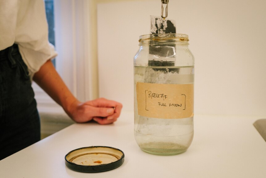 Artist Sammy Hawker dips a film negative in a jar of saltwater.