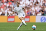 An England women;'s footballer extends her right foot to pass the ball along the ground to a teammate during a big game.