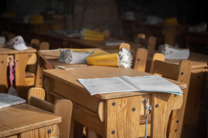 An empty classroom with open books still on the desks