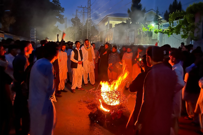 South Indian men stand in a circle around a bonfire at night on city street