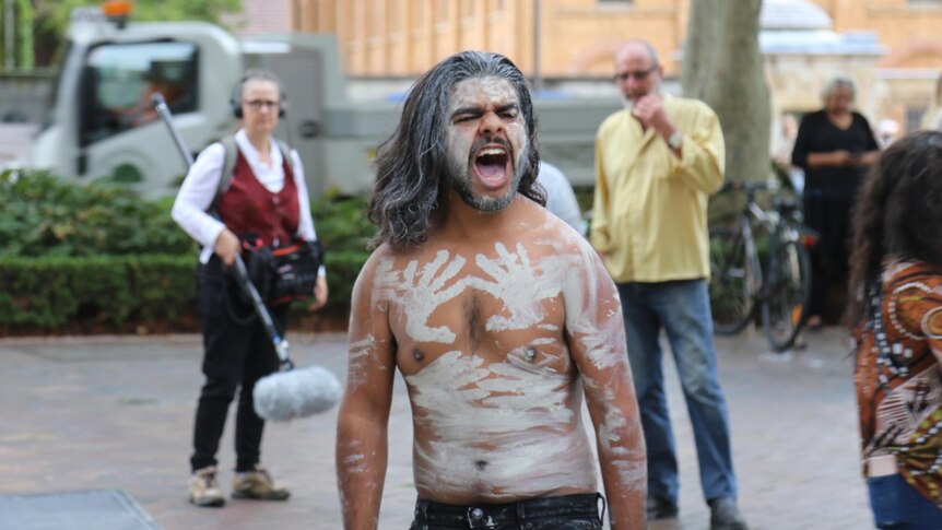 A man covered in white body paint outside a court building.