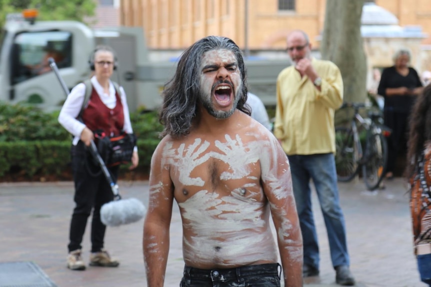 A man covered in white body paint outside a court building.