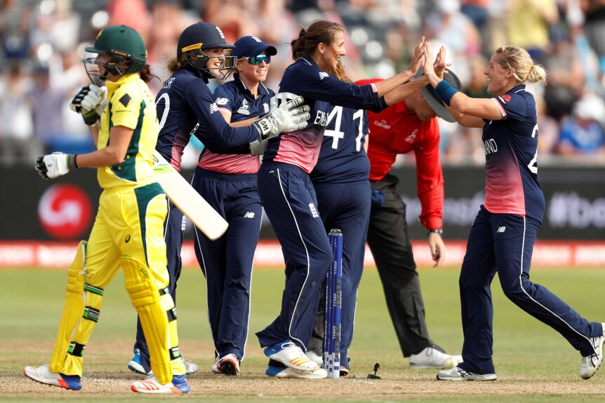 An Australian batter leaves the field as England players celebrate their win.