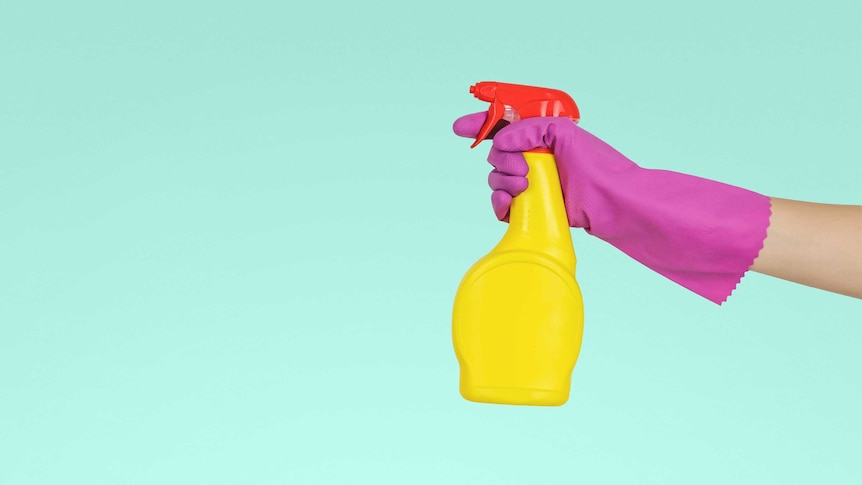 Pink gloved hand holding yellow plastic spray bottle.