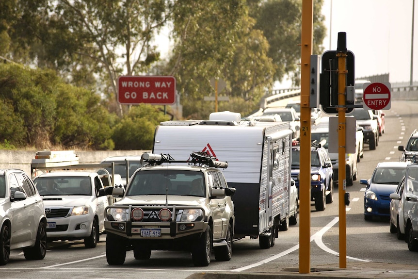 A four-wheel drive towing a caravan stationary at traffic lights as cars bank up behind it.