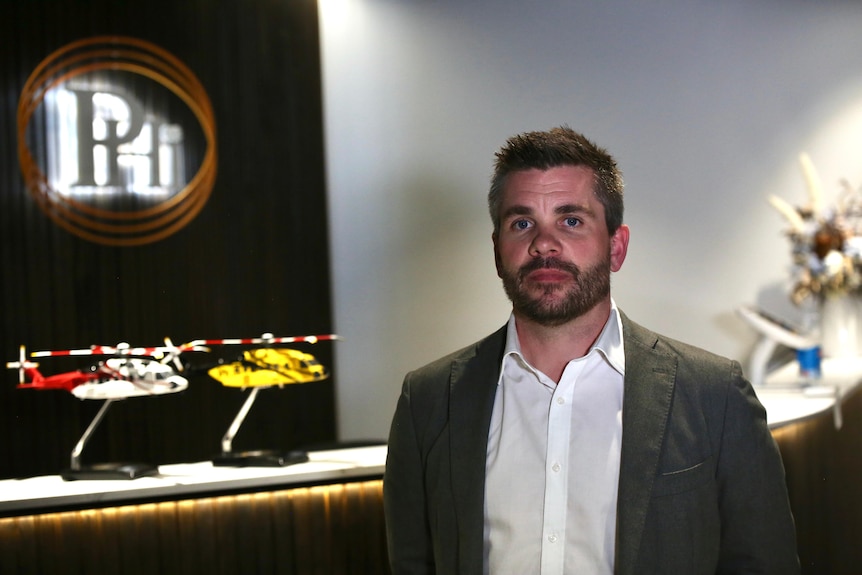 A man in a jacket and shirt stands next to some model helicopters. 