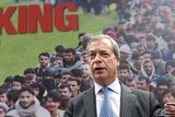 Nigel Farage stands in front of a large billboard with the words Breaking Point and an image of immigrants.