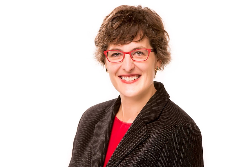 A woman with red-framed glasses smiles at the camera, white background.