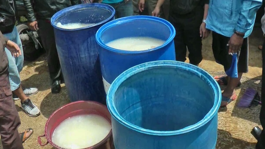 Drums of liquid are seen on the ground as police raid sellers of bootleg alcohol.