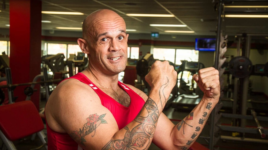 A man holding his fists up showing tattoos with aboriginal designs and an aboriginal flag