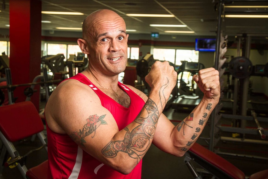 A man holding his fists up showing tattoos with aboriginal designs and an aboriginal flag