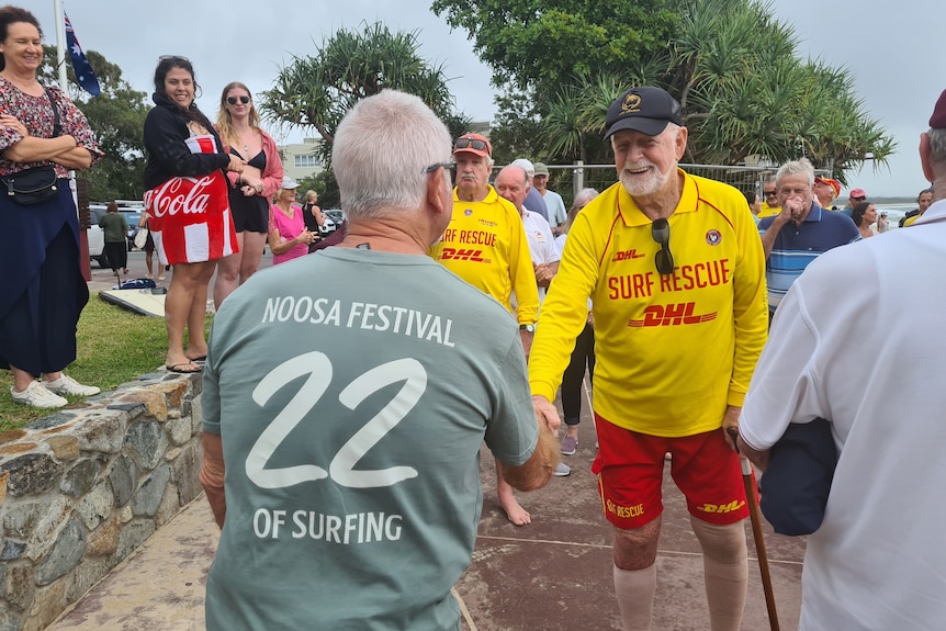 A man in a pale green shirt shakes the hand of a life saver as people look on and smile