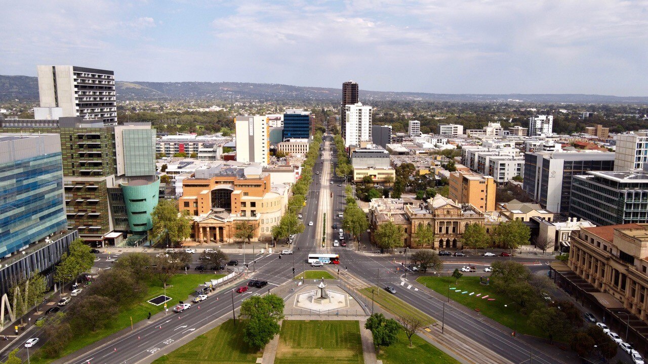 A shot of Adelaide's CBD taken by drone, with a park in the foreground, buildings behind and hills in the background.