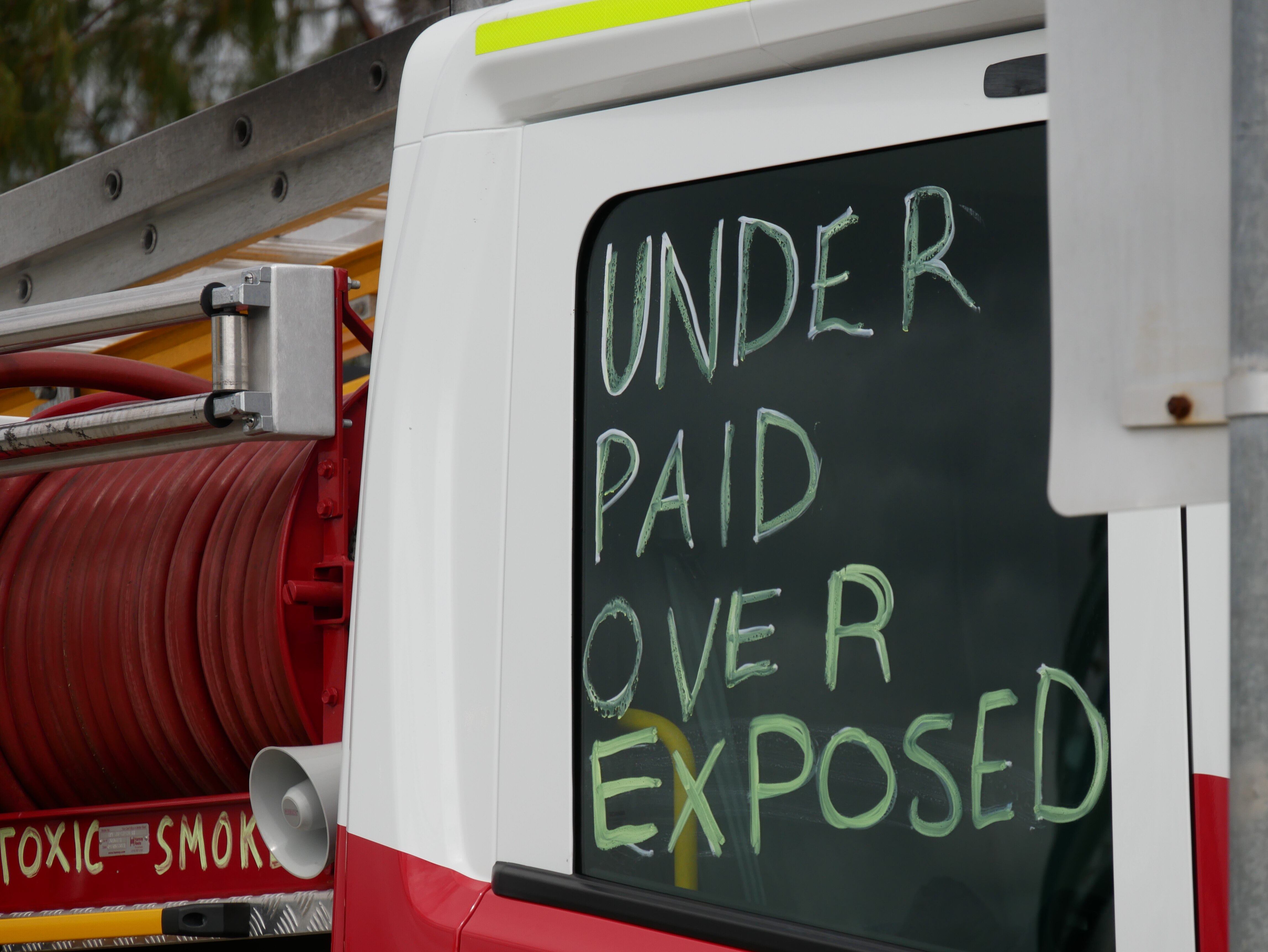 “Mal pagado, sobreexpuesto” está escrito en la ventanilla de un camión de bomberos.