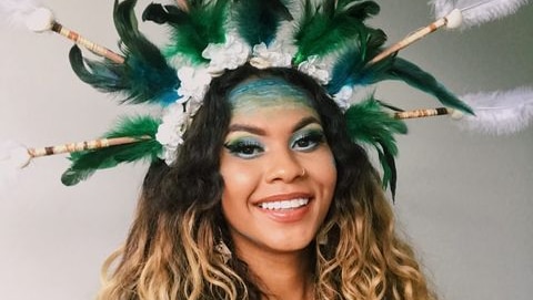 A young woman with wavy blonde hair wears a traditional green and white Torres Strait headdress.