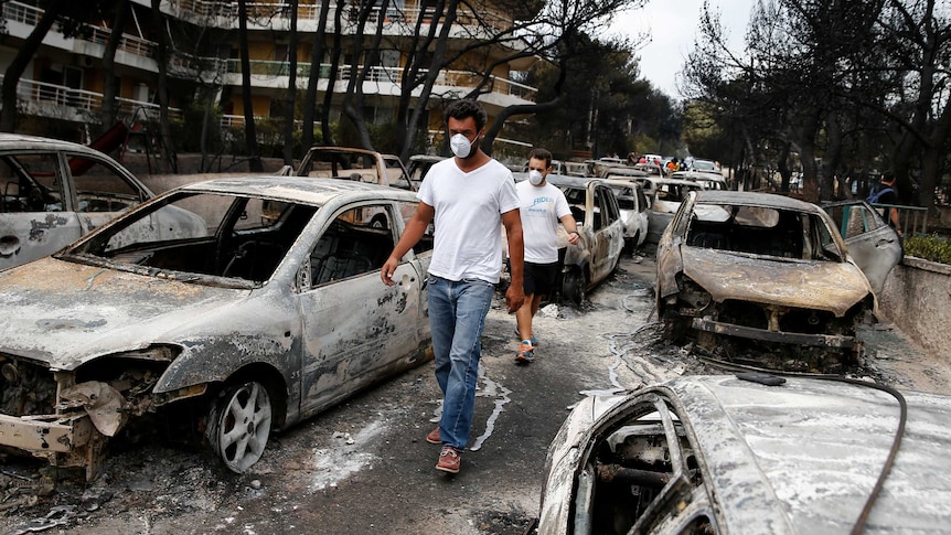 Two men wearing masks walk on a street packed with burnt cars.