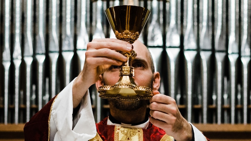 Priest holding up a golden cup of wine at an altar.