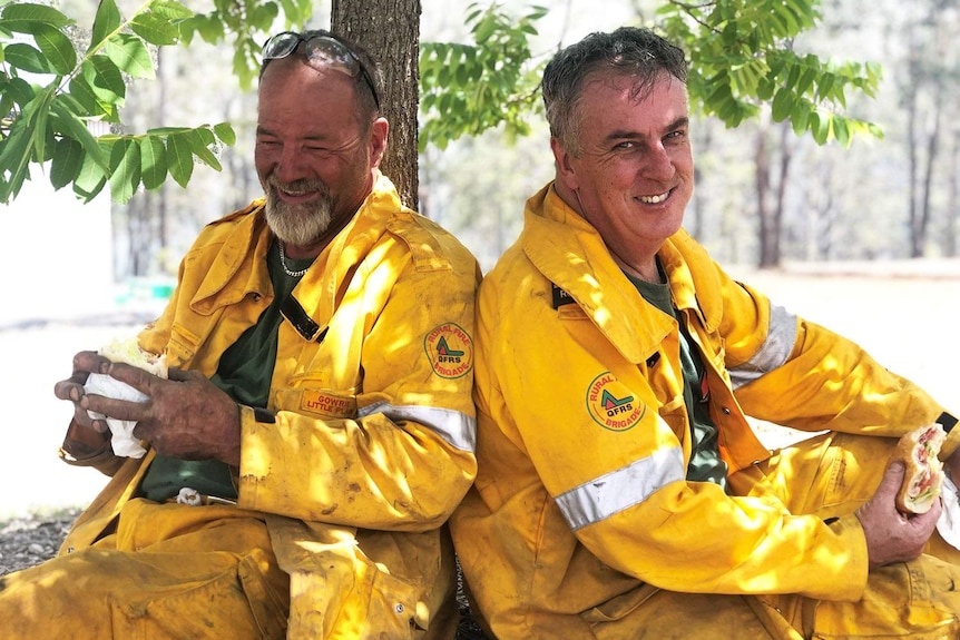 Firefighters Craig Partridge and Ken Dudley smile as they take a rest sitting under a tree.