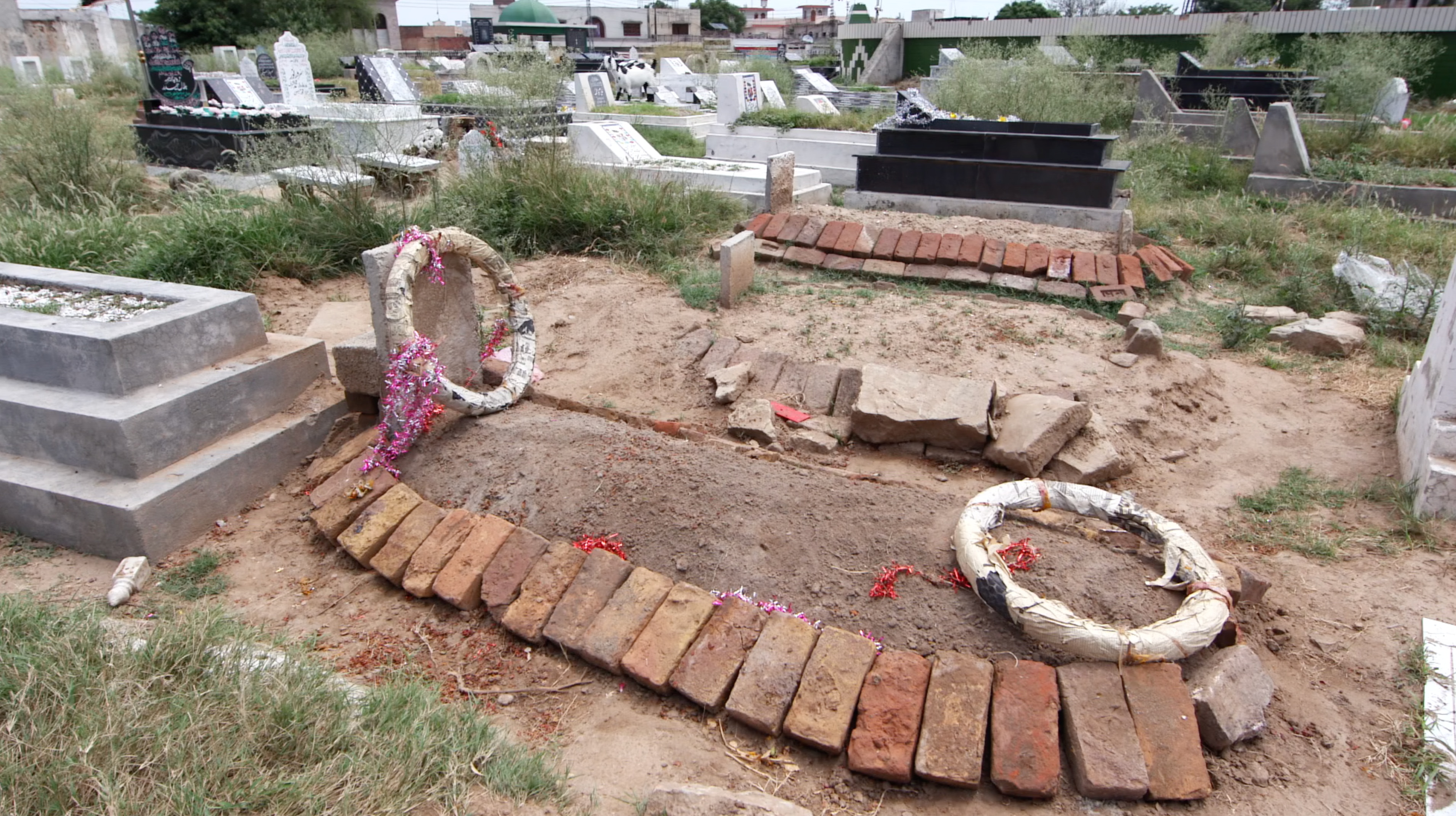 A makeshift grave in a graveyard is framed by bricks and wreaths