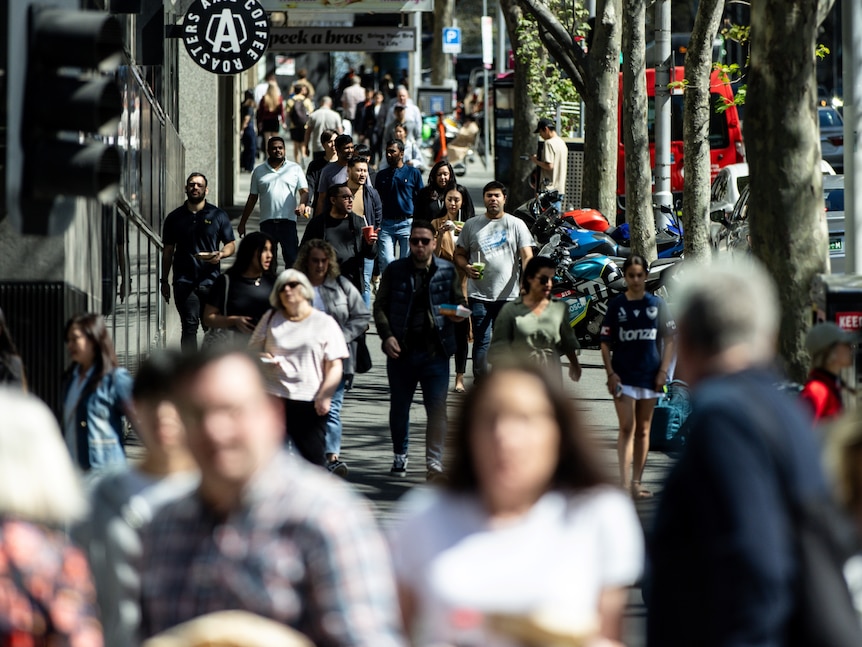 A crowd of people walking along a street in a central business district in Melbourne on a sunny day.