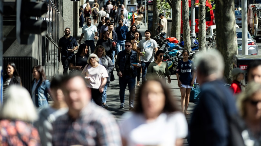 A crowd of people walking along a street in a central business district in Melbourne on a sunny day.