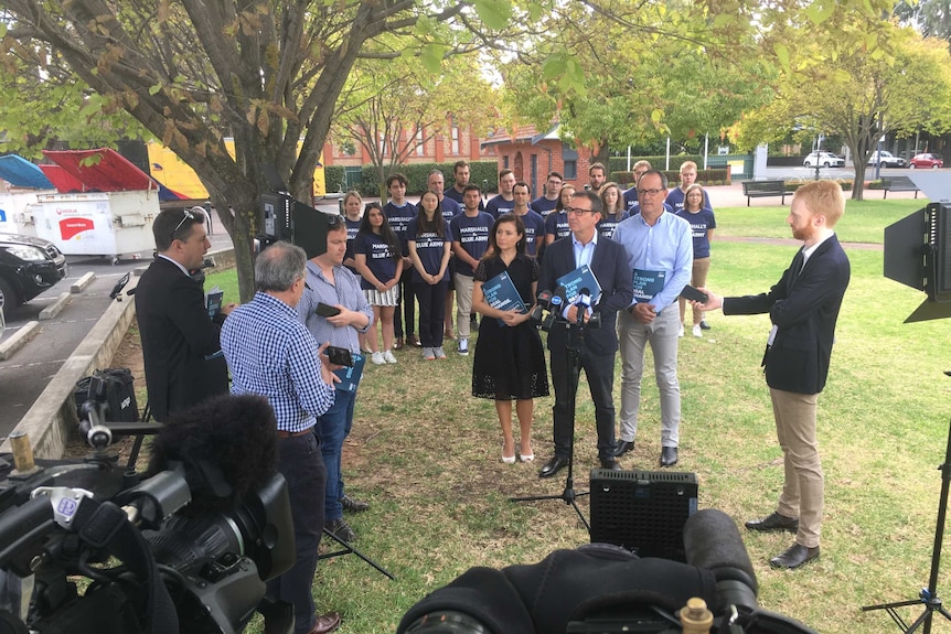 Media gathered to hear three politicians speak in a park.