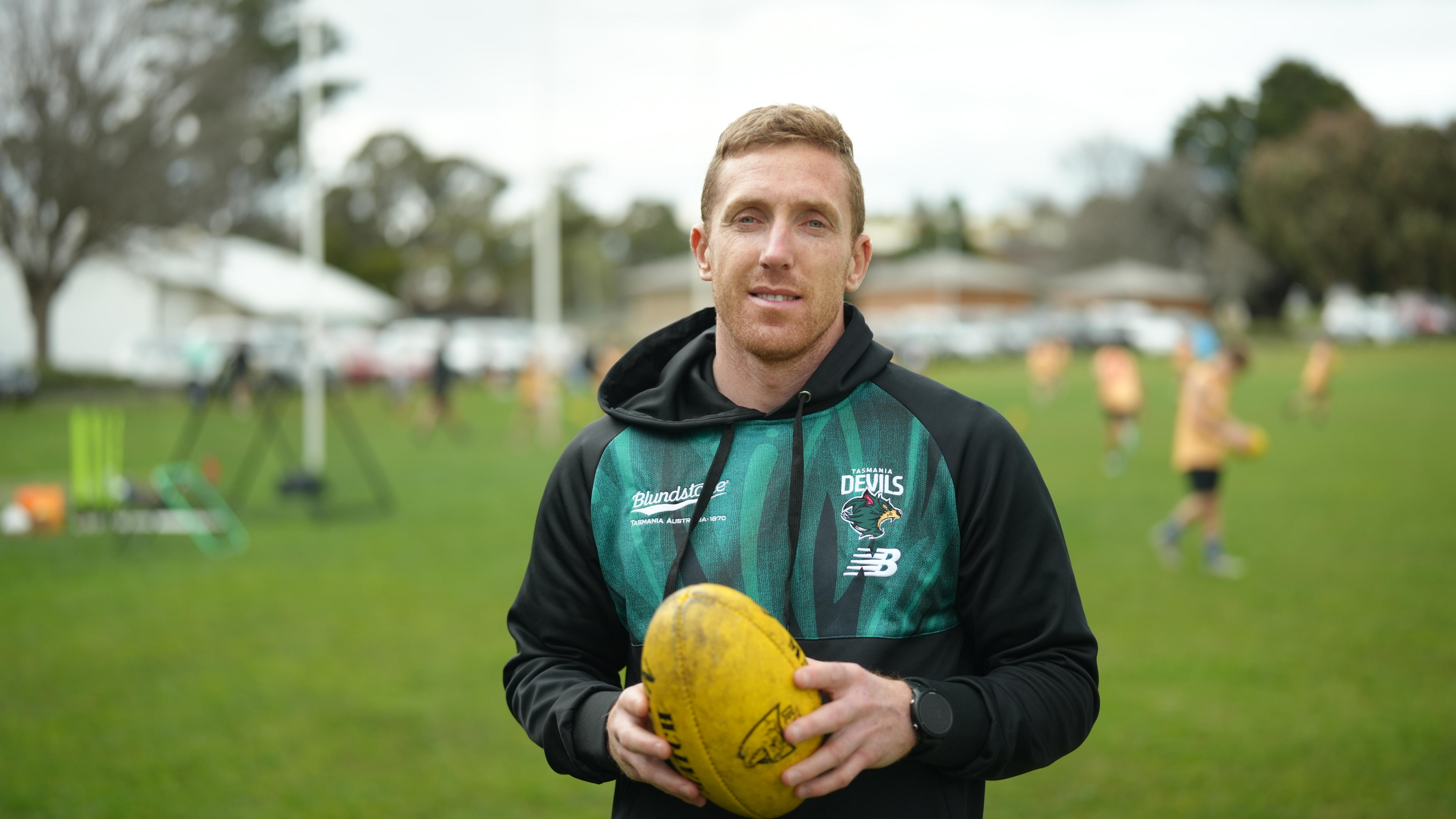 A man wearing a black and green hoodie smiling at the camera holding a yellow football.