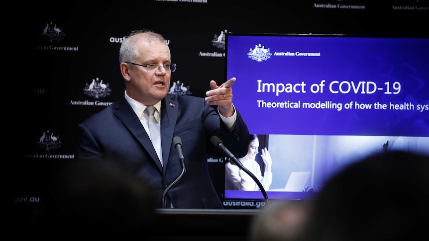 Scott Morrison stands in front of a screen with data about coronavirus. He points into the distance