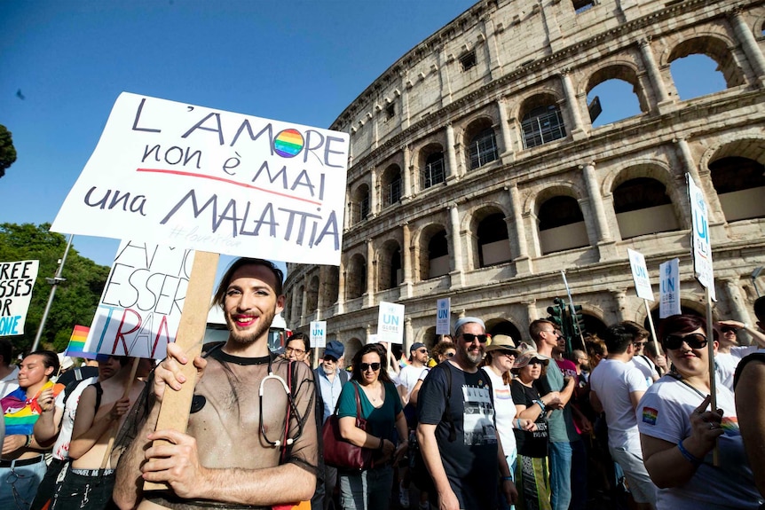 A man in a crowd holds up a sign in front of Rome's  Colosseum.