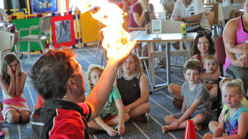 Man kneels in front of group of children with a fireball in his hand