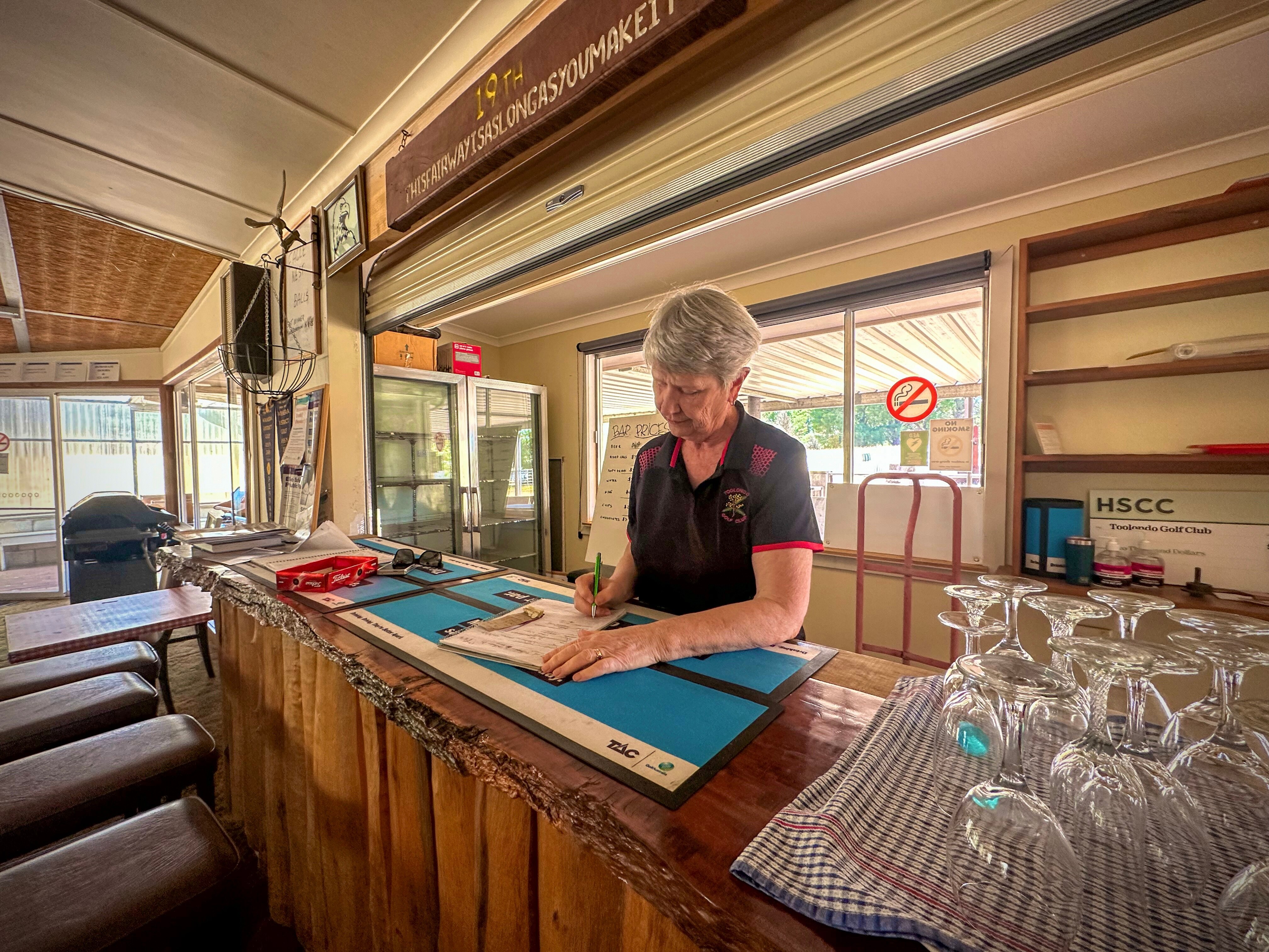 Woman with short grey hair signing a document at an outback bar inside a building
