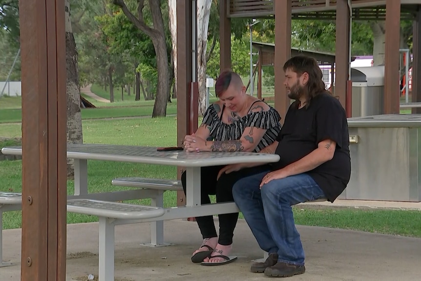 A man and woman sit at a picnic table in a park.