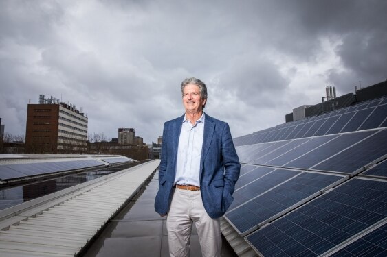 A man with grey hair and wearing a blue suit jacket on a rooftop with solar panels