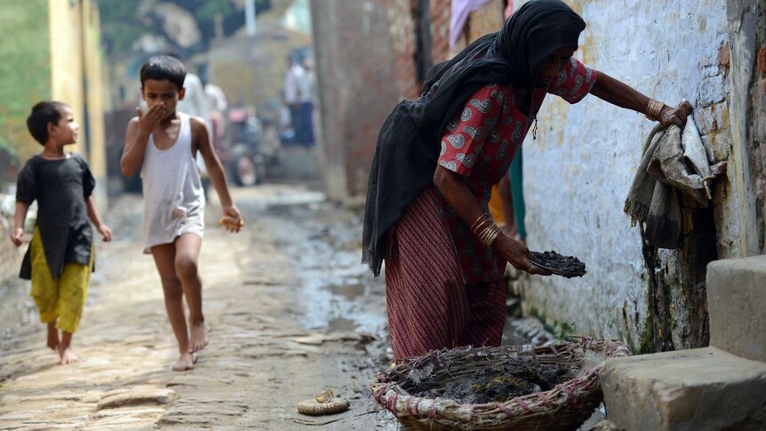 A child covers his nose as he passes a female manual scavenger cleaning a toilet.