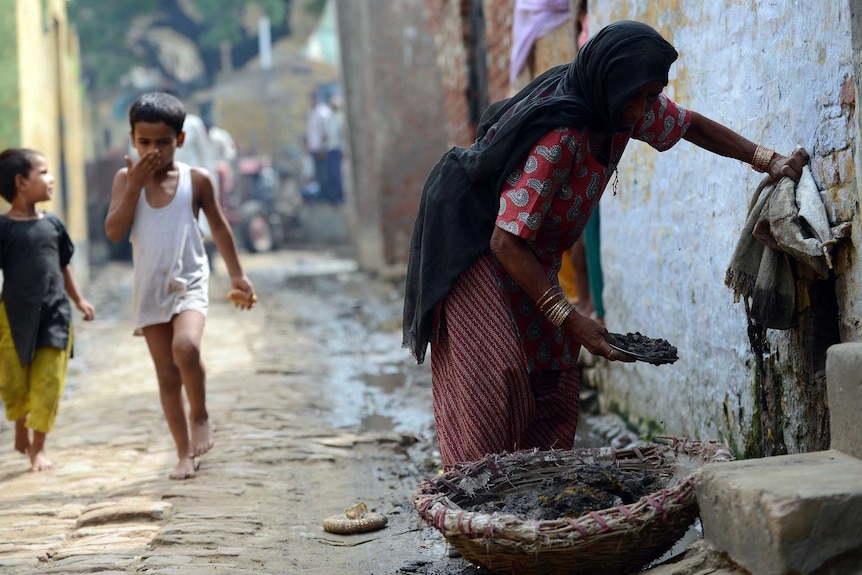 A child covers his nose as he passes a female manual scavenger cleaning a toilet.