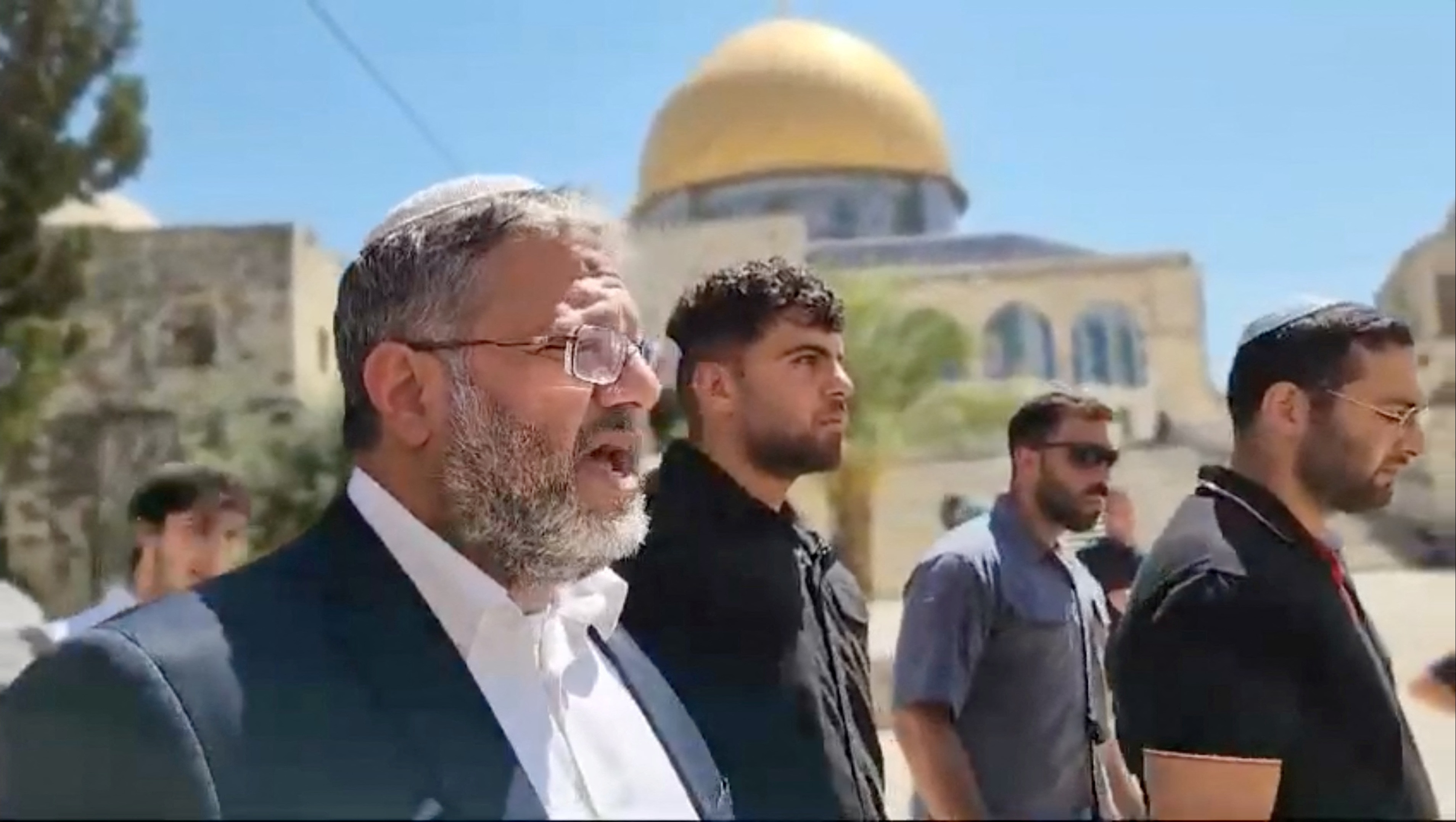 Men walking with the golden dome of the rock behind them.