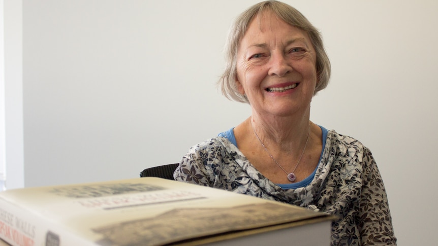 A woman sits on a char next to a large book