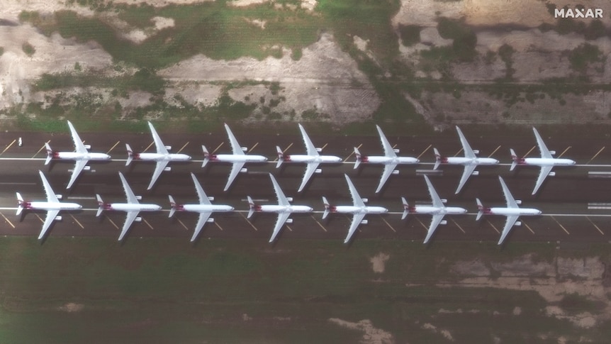 A satellite image shows two parallel rows of passenger planes sit parked on a runway