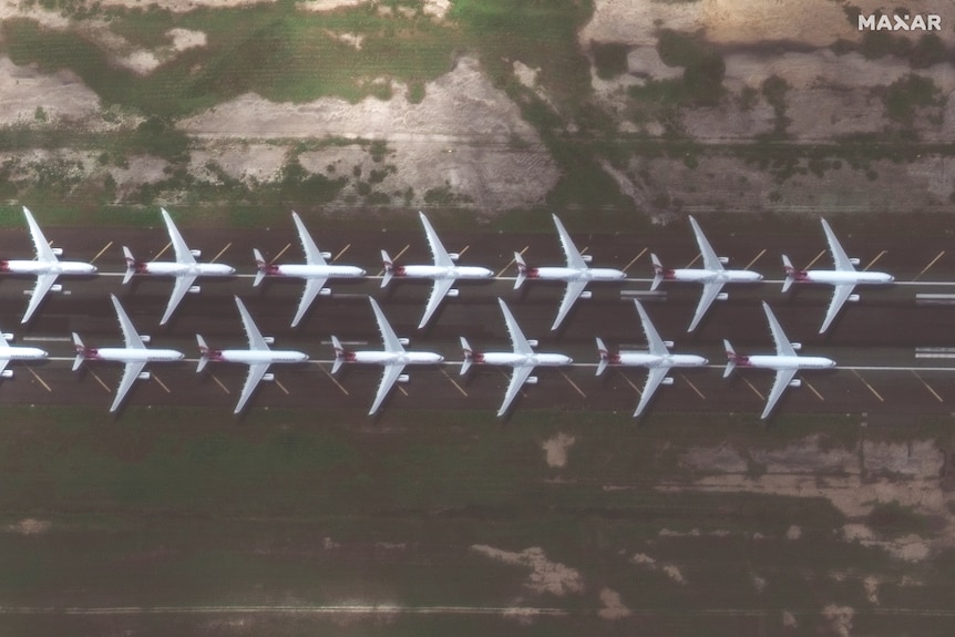 A satellite image shows two parallel rows of passenger planes sit parked on a runway
