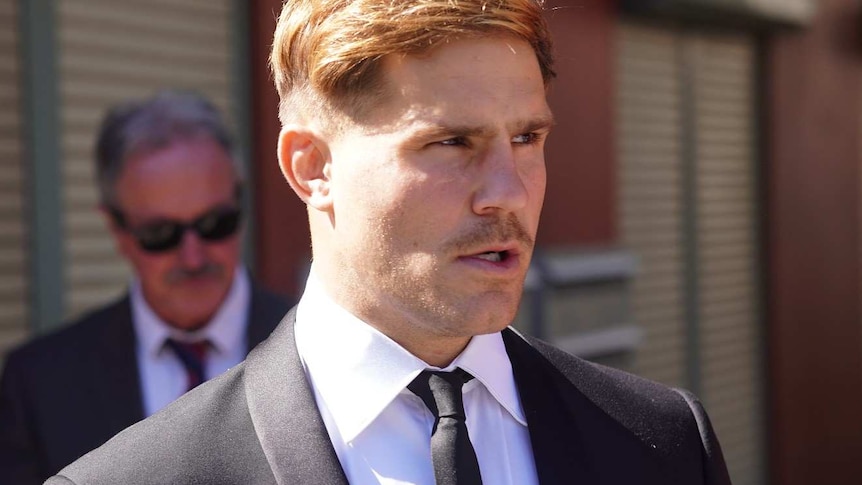 A young man in a dark suit walks towards a court building.