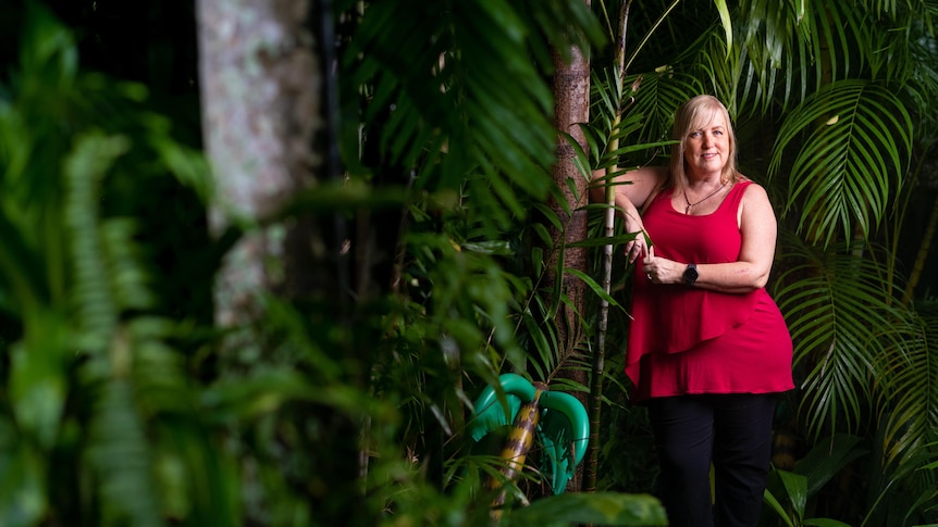 Annemarie Lloyd stands in her garden among green tropical plants.