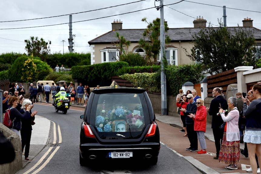 People stand by the side of the road as a hearse carrying the coffin of Sinead O'Connor passes.