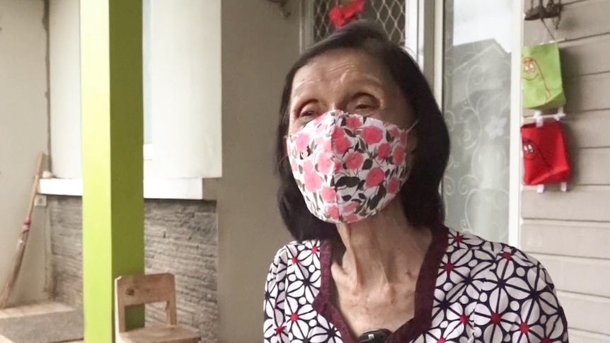 A woman with dark hair and wearing a floral mask and patterned shirt looks at the camera.