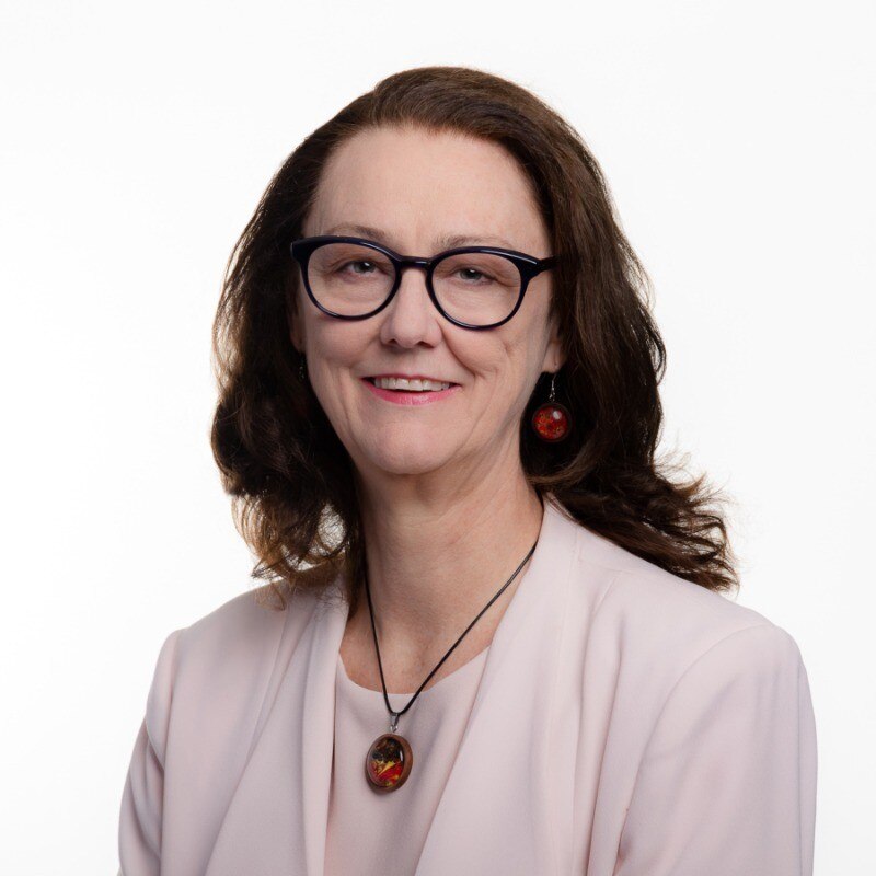 A portrait of an older woman wearing glasses and a pink top.
