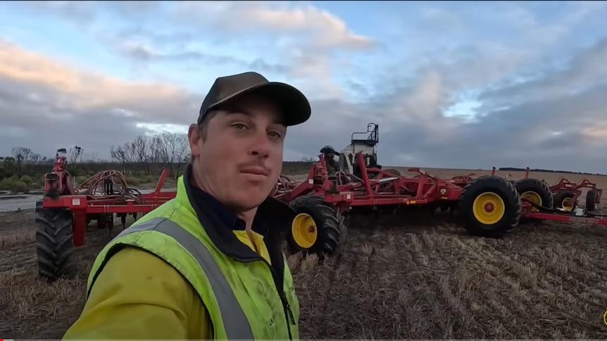 farmer stands in front of farming equipment
